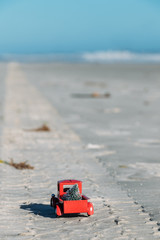 A small red truck hauling a Christmas tree drives down tire tread on New Smyrna Beach Florida.