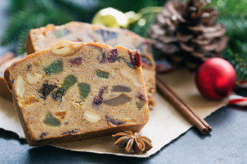 Sweet fruit cake slices on brown paper put on black granite table in close up view with Christmas decoration. Traditional rum fruit cake for Christmas celebrate festival. Homemade bakery concept.