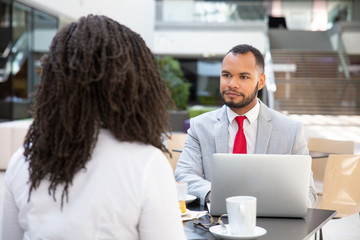 Customer and consultant talking over cup of coffee in office lobby. Business man and woman sitting in cafe, using laptop, talking. Partners meeting concept