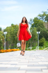 Young beautiful model in red dress walking on the summer street