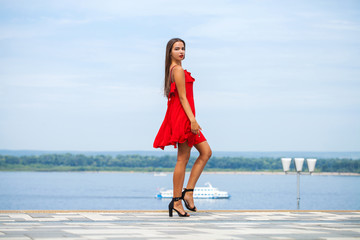 Young beautiful model in red dress walking on the summer street