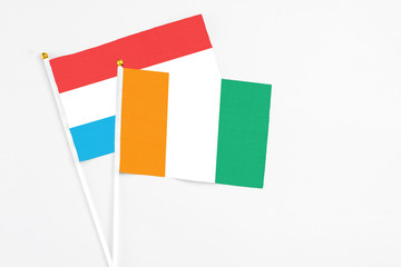 Cote D'Ivoire and Luxembourg stick flags on white background. High quality fabric, miniature national flag. Peaceful global concept.White floor for copy space.