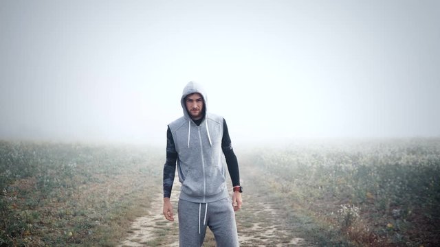 Sporty fit young man walking into the frame in the middle with foggy background, motivational