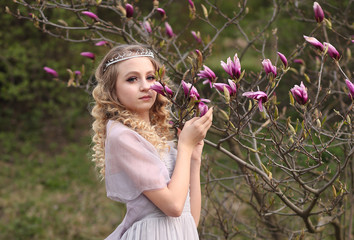 Fototapeta premium young beautiful girl in a light lilac dress in the garden where magnolias bloom