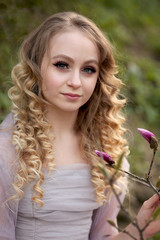 Naklejka premium young beautiful girl in a light lilac dress in the garden where magnolias bloom
