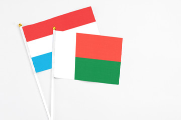 Madagascar and Luxembourg stick flags on white background. High quality fabric, miniature national flag. Peaceful global concept.White floor for copy space.