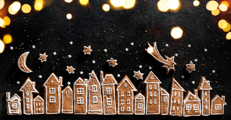 Christmas background, gingerbread  cookies houses, fresh yew branches, gingerbread stars and twinkling lights on a black  background. Christmas gingerbread town