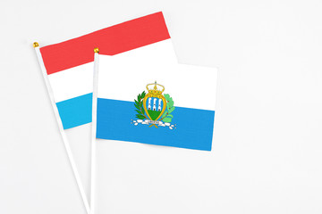 San Marino and Luxembourg stick flags on white background. High quality fabric, miniature national flag. Peaceful global concept.White floor for copy space.