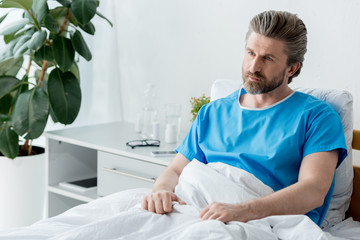 patient in medical gown sitting on bed and looking away in hospital