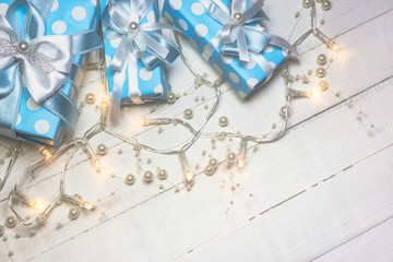 Blue gift boxes and lights with pearls on white wooden background