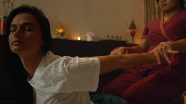Asian Woman performs Traditional Thai Massage to beautiful European Woman. Rehabilitation and Treatment after Injuries with the help of Massage. Relax and Rest from massage of Legs, Arms and Back.