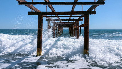 Waves breaking on a rusty metal pier. Seascape on a sunny day.