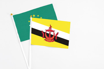 Brunei and Macao stick flags on white background. High quality fabric, miniature national flag. Peaceful global concept.White floor for copy space.