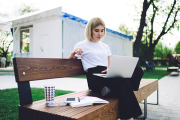 Young female student with laptop and notepad on bench