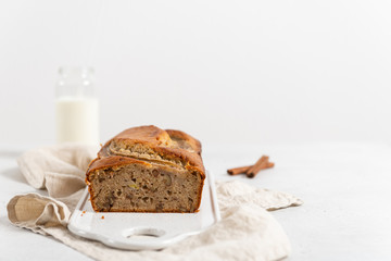 Homemade delicious banana cake with walnuts and cinnamon and a bottle of milk on white concrete background. Side view, copy space. Bakery banner, recipe. Selective focus