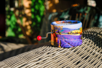 Cute music box with Provence landscape  on wicker surface in bright sun. Bright small hurdy-gurdy....