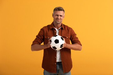 displeased man holding football isolated on orange