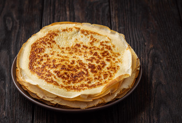 Homemade stack of crepes, on dark wooden background.