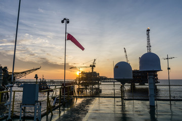 Sunset at oil field with communication dome antenna and wind sock on board a construction barge