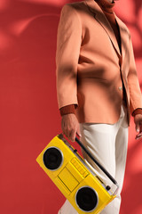 cropped view of stylish man holding yellow boombox on red with shadows