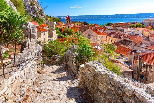 Sunny red roofs, Old city street with stone stairs and Church of St Michael in town and port Omis, popular tourist spot in Croatia