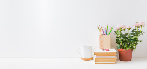 Home office, interior for bloggers workplace with roses in a pot, books, white mug, office supplies