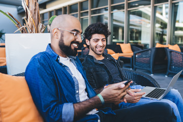 Laughing ethnic men with gadgets in cafe