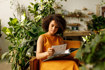 Woman florist working. Young female reading from a book in the small botanical studio.