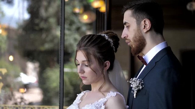 thoughtful couple poses for wedding photo shoot near window with yard blurry reflection slow motion closeup