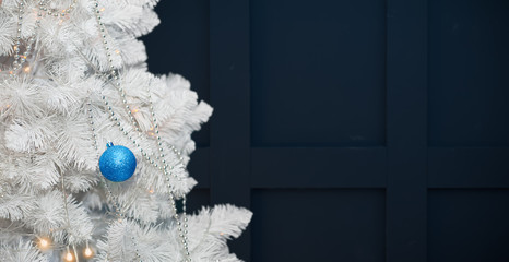 A snow-white Christmas tree decorated with garlands, silver beads, and a blue ball, on a dark background. Minimalistic Christmas background.