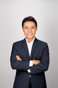 Happy Asian young businessman standing cross-armed on white background