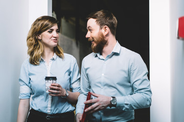 Two smiling office workers in formal wear enjoying communication during coffee break, cheerful male and female colleagues laughing from funny joke on business subject in modern company interior