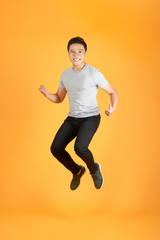 Fototapeta na wymiar Energetic happy young Asian man in casual clothes jumping, studio shot isolated in orange background