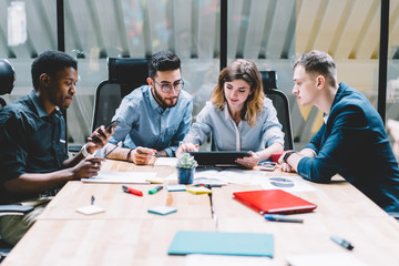 Group of caucasian creative workers discussing project ideas and researching business solutions while sitting at office table during meeting. four young employees brainstorming and sharing opinions