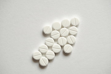 Abstract signs and symbols of growth, business development, profit. White pharmaceutical drug pills stacked on a flat white surface in the shape of an arrow pointing up and forward.