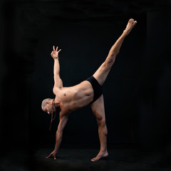 Graceful Hispanic man practicing yoga asana in a black studio. Half Moon pose Ardha Chandrasana
