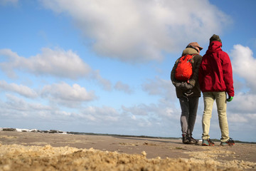 Father and son looking on the water at beautiful weather while standing on the beach spread with foam hills at low tide after a strong storm