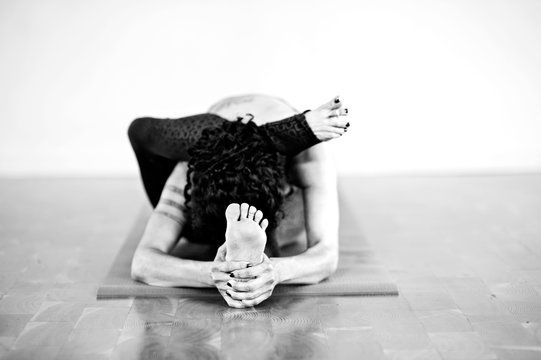 Hispanic yoga woman practicing in studio photographed in black and white. Eka Pada Sirsasana also known as Foot Behind The Head Pose