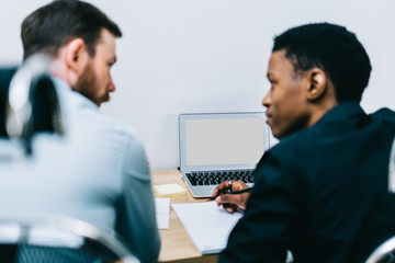 Back view of multicultural colleagues discussing productive strategy of developing business website sitting at laptop device.Selective focus on modern computer with copy space for internet content