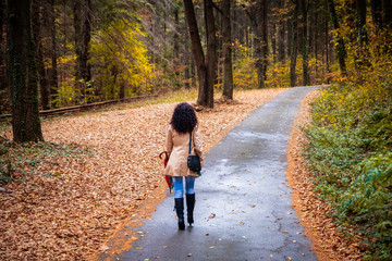 Fototapeta premium Woman walking in the rain on asphalt forest road at autumn. Road next to the Tresnja lake in Serbia.