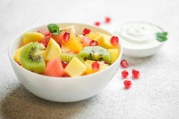 Bowl with homemade fresh fruit salad: mango, grapefruit, pomegranate, kiwi, banana on a light background.