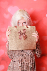 blonde young girl with gift box on red background alone