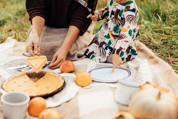 Young Mom with a little cute daughter at an autumn picnic cut a pumpkin tart.