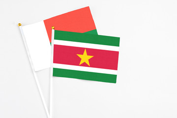 Suriname and Madagascar stick flags on white background. High quality fabric, miniature national flag. Peaceful global concept.White floor for copy space.