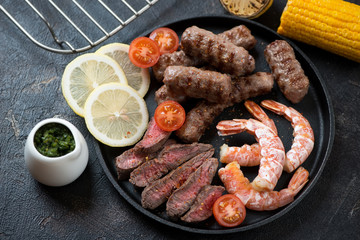 Surf and turf with sliced beefsteak, marbled beef sausages, shrimps, tomatoes, corn, lemon and chimichurri sauce, studio shot