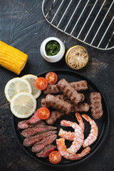 Surf and turf meal with beefsteak, bbq marbled beef sausages and shrimps, flatlay over dark brown stone surface