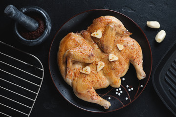 Black plate with georgian traditional roasted chicken tabaka, flatlay over black stone background, studio shot