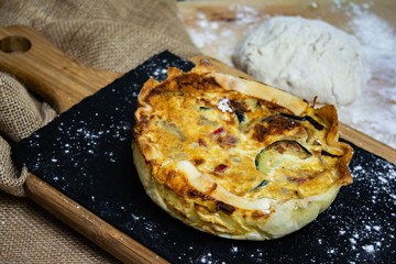 Vegetable quiche on wooden background with flour dough in the background. Typical dish of French cuisine. Vegetarian Food. Homemade food prepared