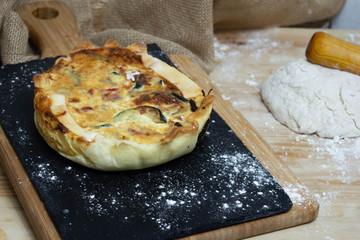 Vegetable quiche on wooden background with flour dough in the background. Typical dish of French cuisine. Vegetarian Food. Homemade food prepared