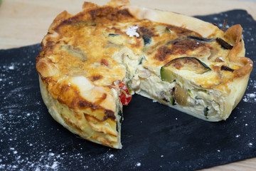 Vegetable quiche on wooden background with flour dough in the background. Typical dish of French cuisine. Vegetarian Food. Homemade food prepared